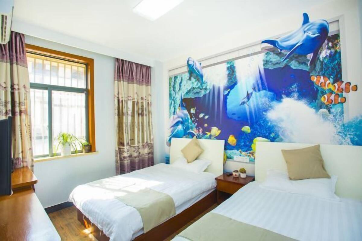 A hotel room with two beds, a large mural of a dolphin and underwater scene, a window with curtains, and a plant on the windowsill.