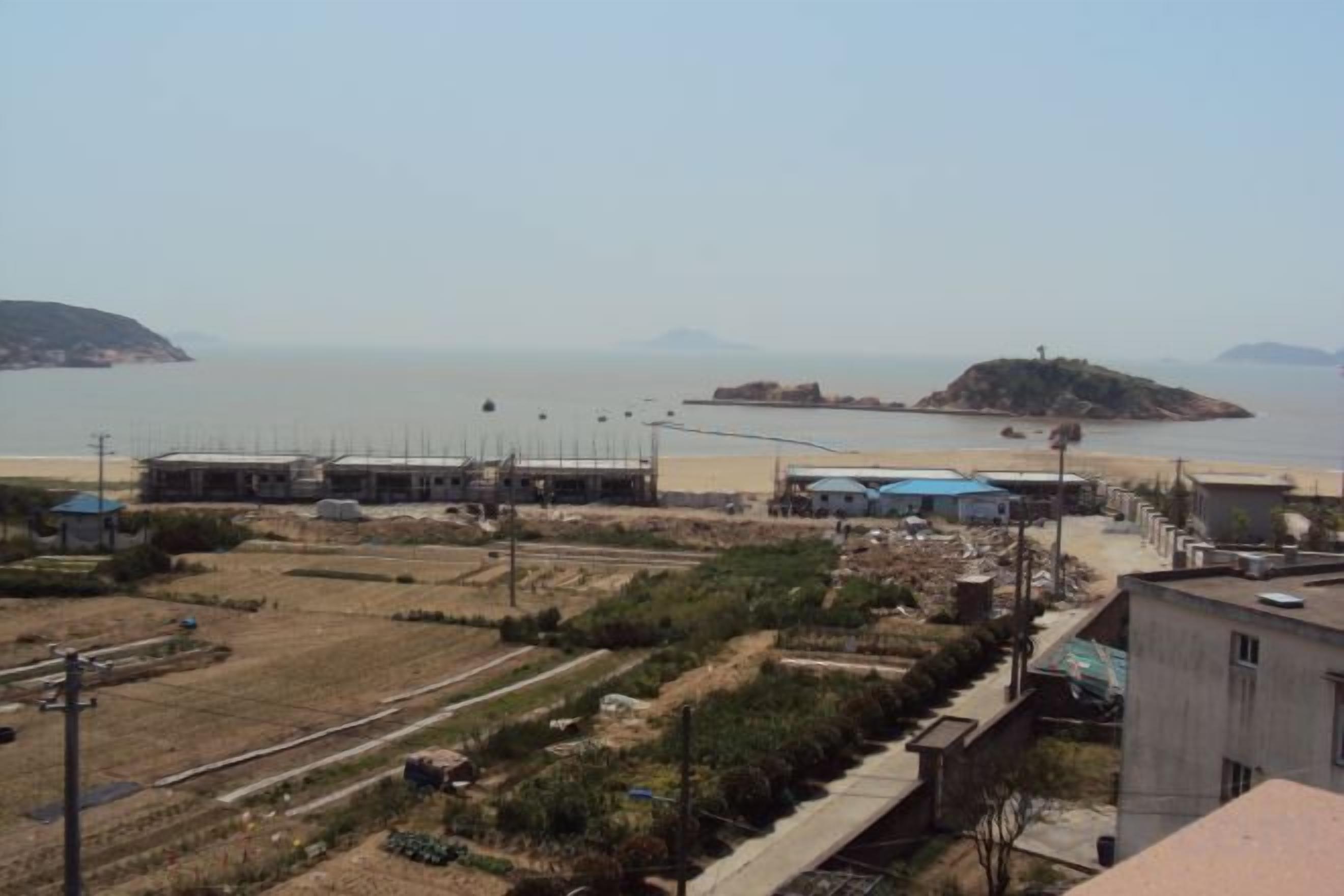 A coastal area with buildings, a beach, and a small island in the distance.
