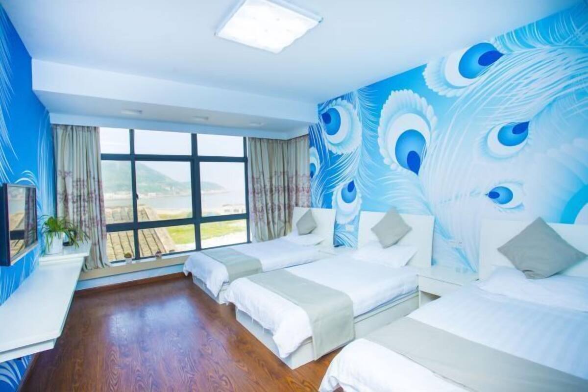 A hotel room with two beds, a large window, and a peacock mural on the wall.