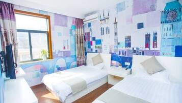 A hotel room with two beds, a window with curtains, a desk, and a wall with architectural prints.