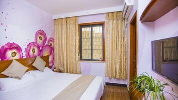 A hotel room with a bed, curtains, a window, an air conditioning unit, and a potted plant.