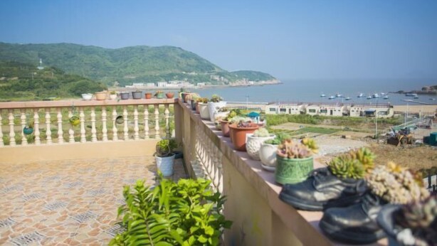 A balcony with potted plants overlooking a coastal area with boats and a hilly landscape. - Caiyuan Bihai Yuntian Hotel (Shengsi)