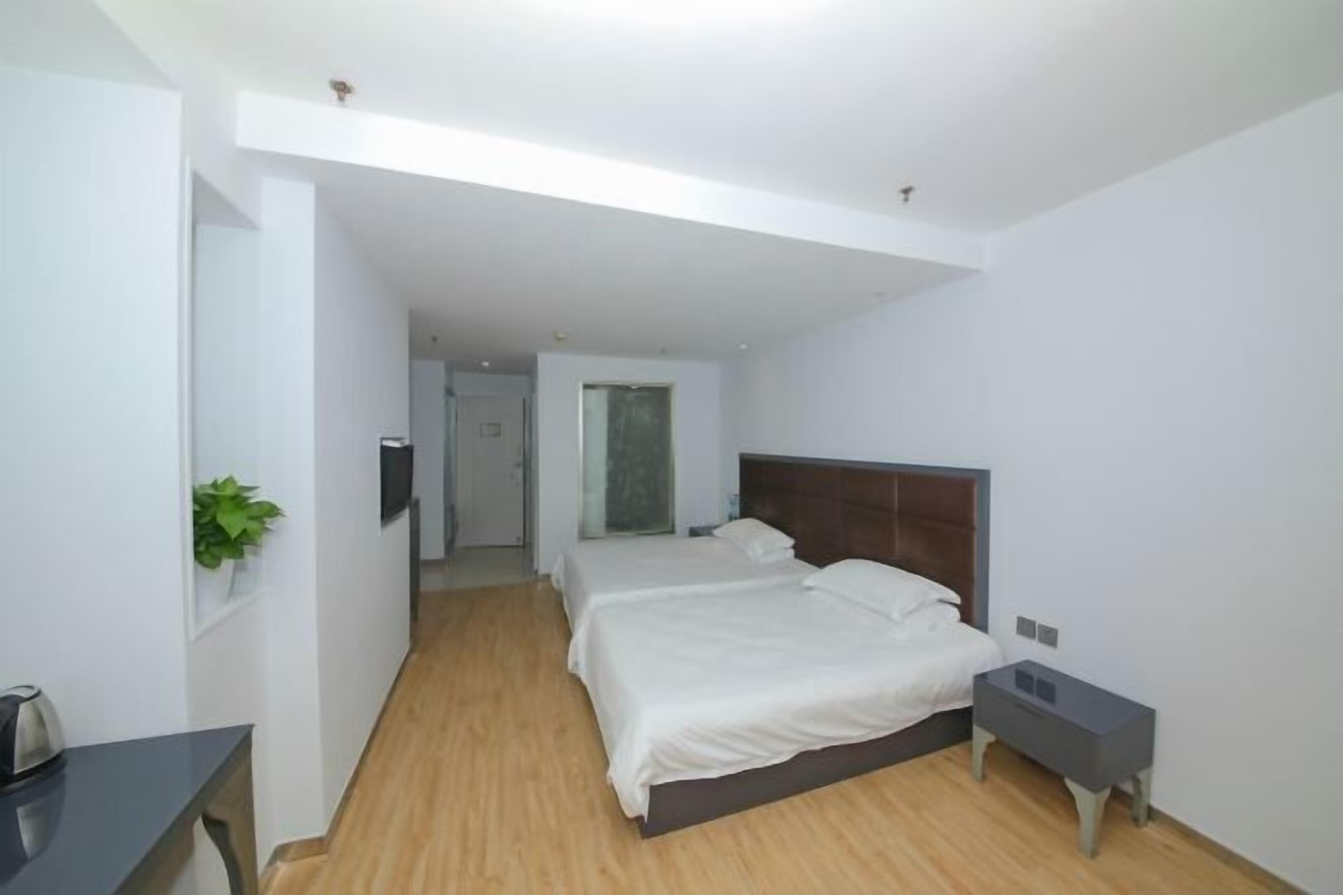 A hotel room with two beds, a desk, a nightstand, and a plant.