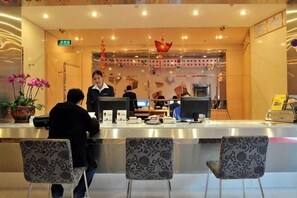 Et hotellets receptionsområde med skranke, to mønstrede stole og en potteplante.