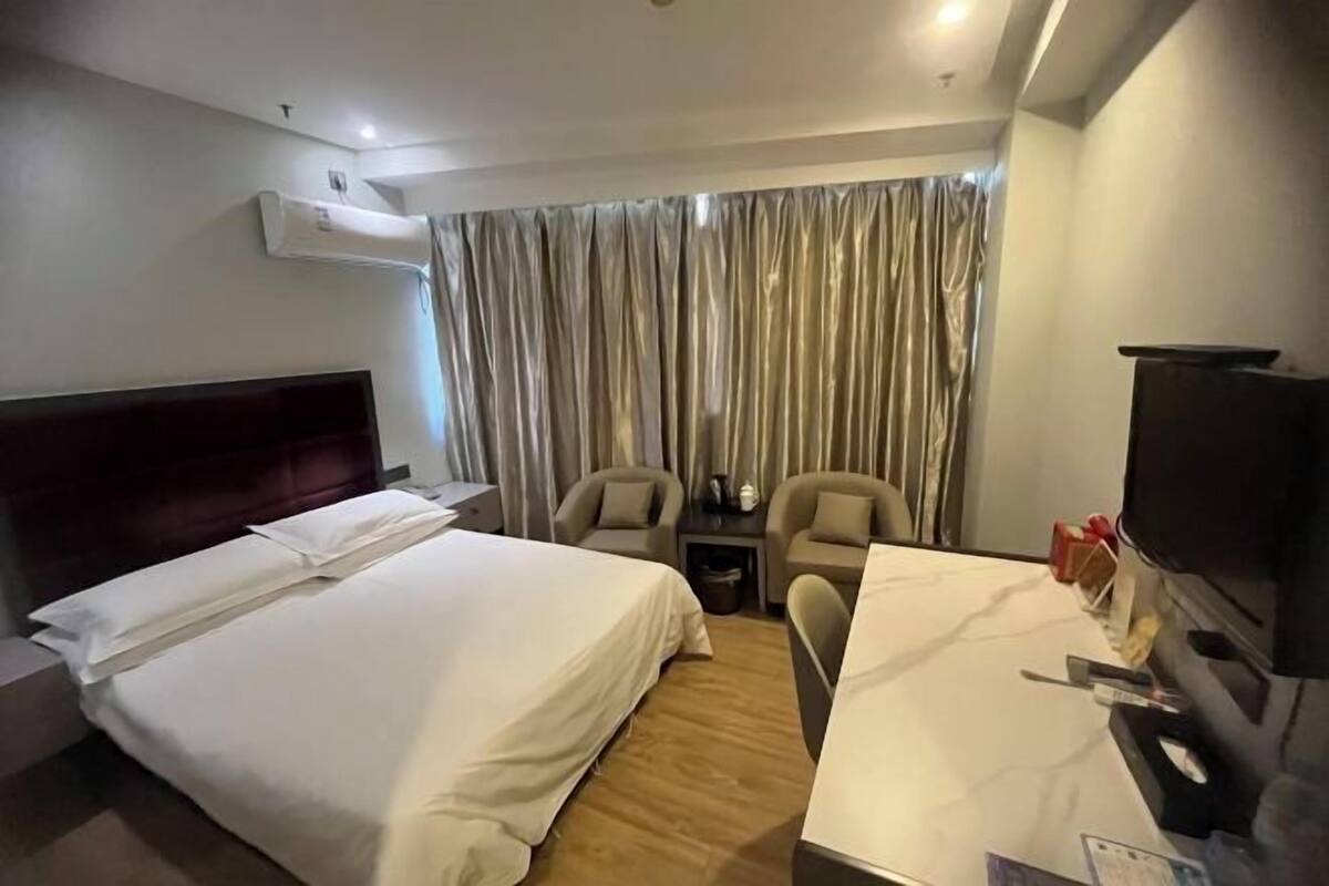 Ein Hotelzimmer mit Bett, Schreibtisch, Stuhl, Fernseher und Vorhang.