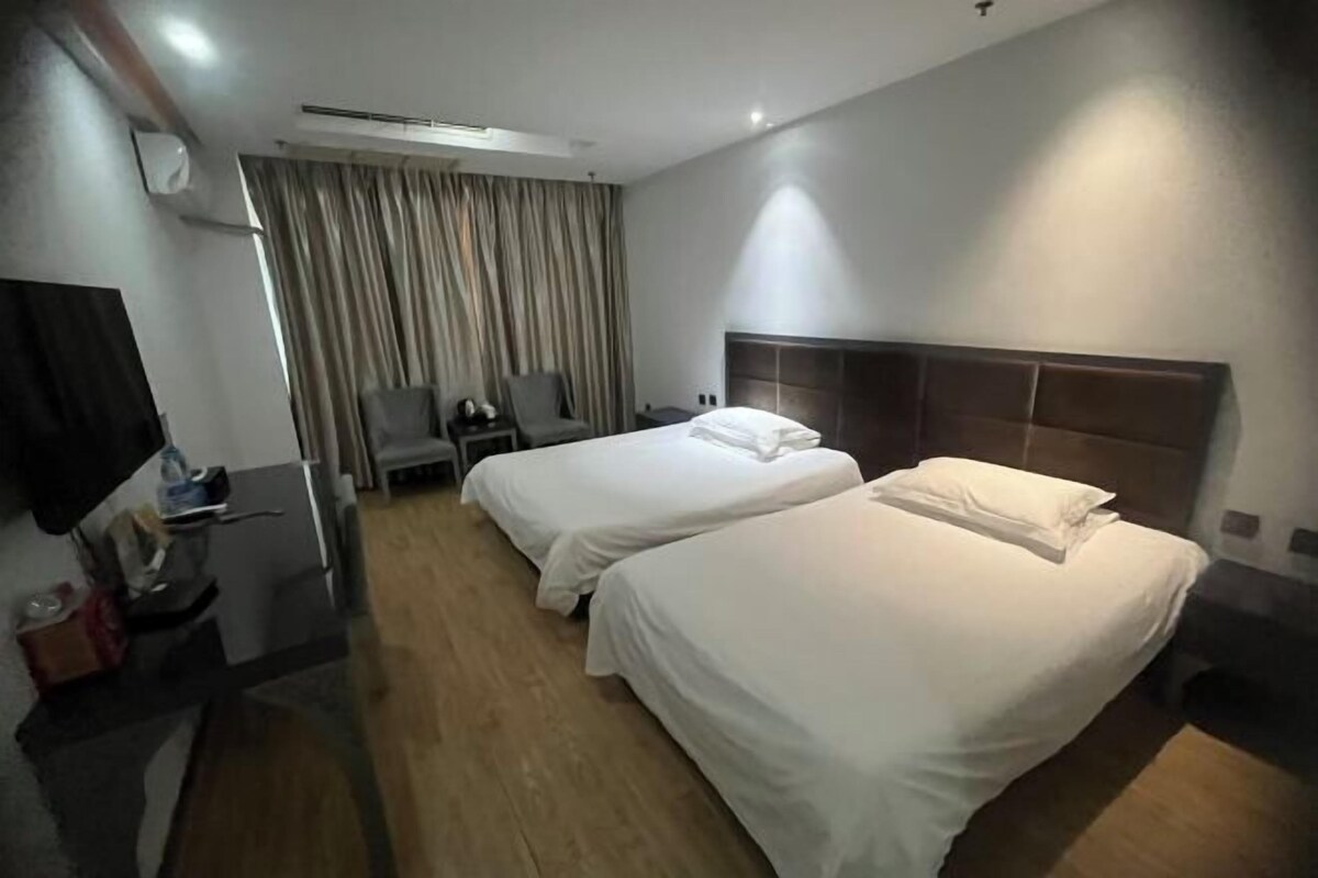 A hotel room with two beds, a desk, a chair, and a TV.