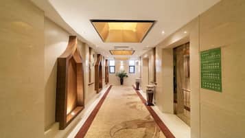 A hotel corridor with a carpeted floor, recessed lighting, and a green sign on the wall.