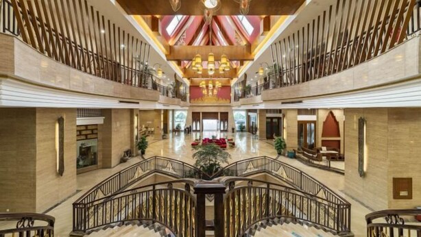 Un vestíbulo espacioso con una escalera central, suelos de mármol y un techo decorativo.