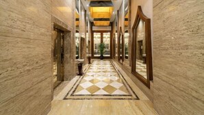 Un pasillo con paredes de mármol y suelo a cuadros, que conduce a una puerta de madera grande.