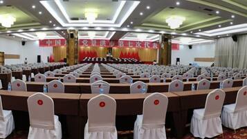A conference room with rows of tables and chairs, a stage with a banner, and a chandelier.
