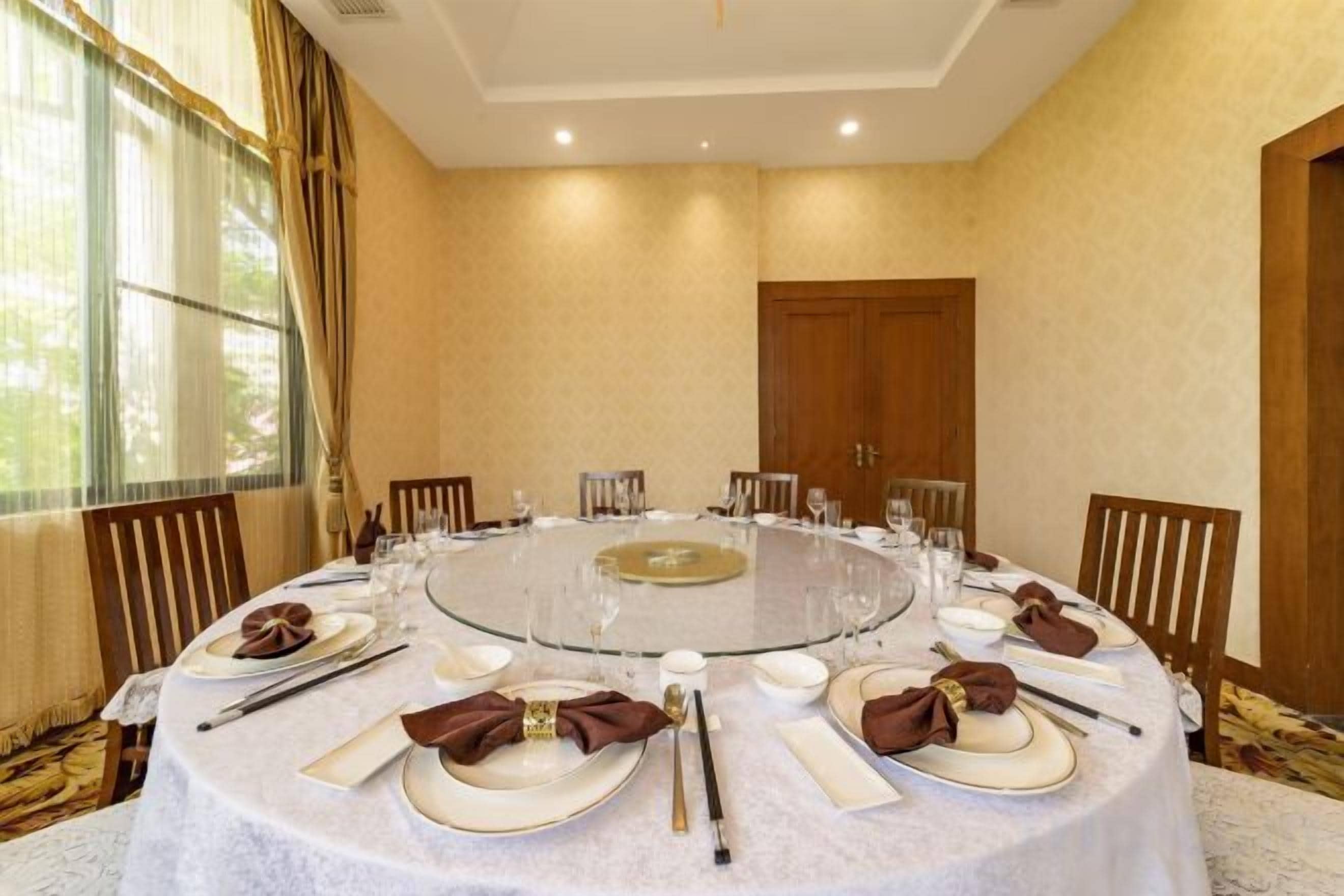 A round table with a glass top, surrounded by chairs, set with white tablecloths, plates, and silverware.
