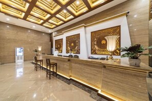 Zona de recepción de un hotel con mostrador de mármol, dos sillones y paneles decorativos en la pared.