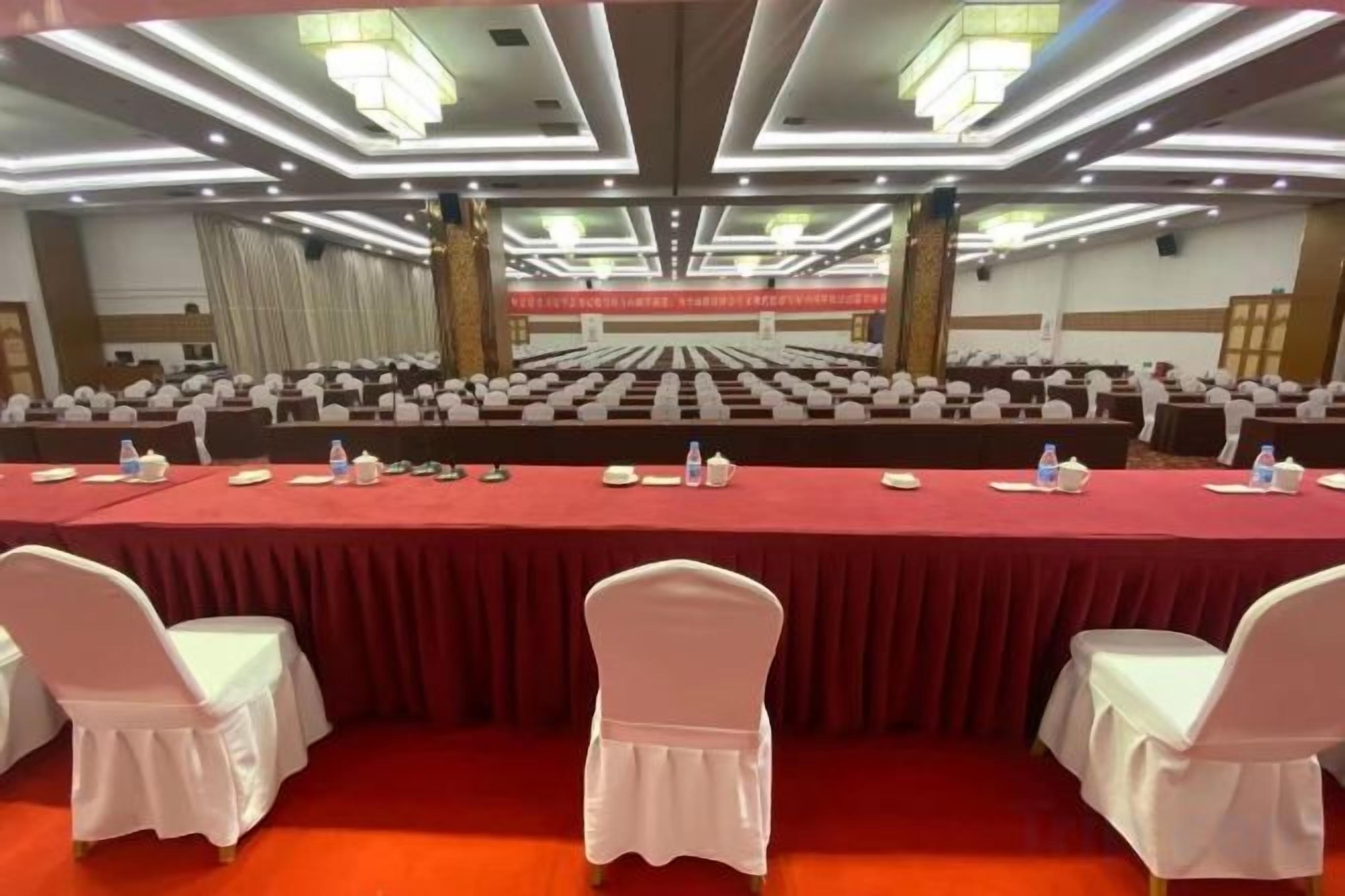 A conference room with rows of tables and chairs, a red tablecloth, and a chandelier.
