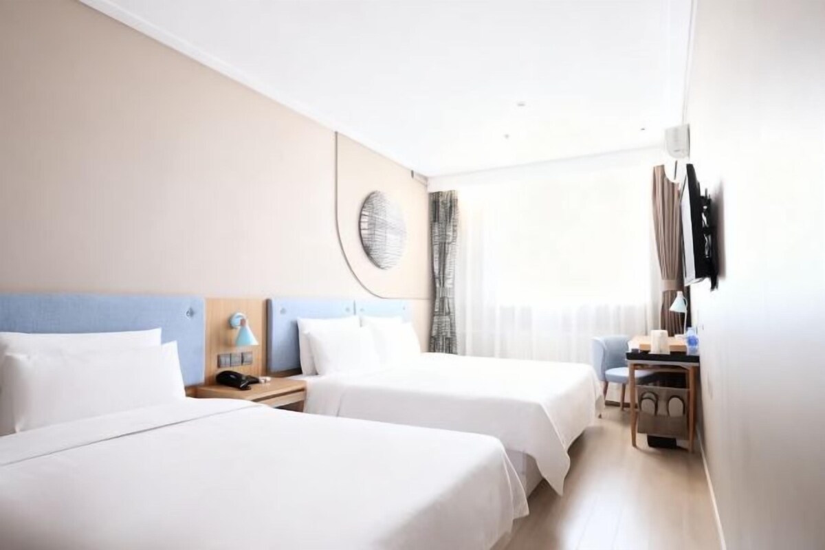 A hotel room with two beds, a desk, a chair, a TV, and a window with curtains.