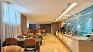 Zona de comedor de hotel moderna, con mesas y sillas, una barra con mostrador de vidrio y una pared de azulejos azules.
