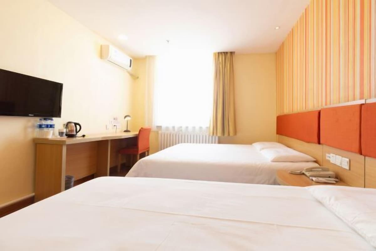 A hotel room with two beds, a desk, a television, and a window with curtains.