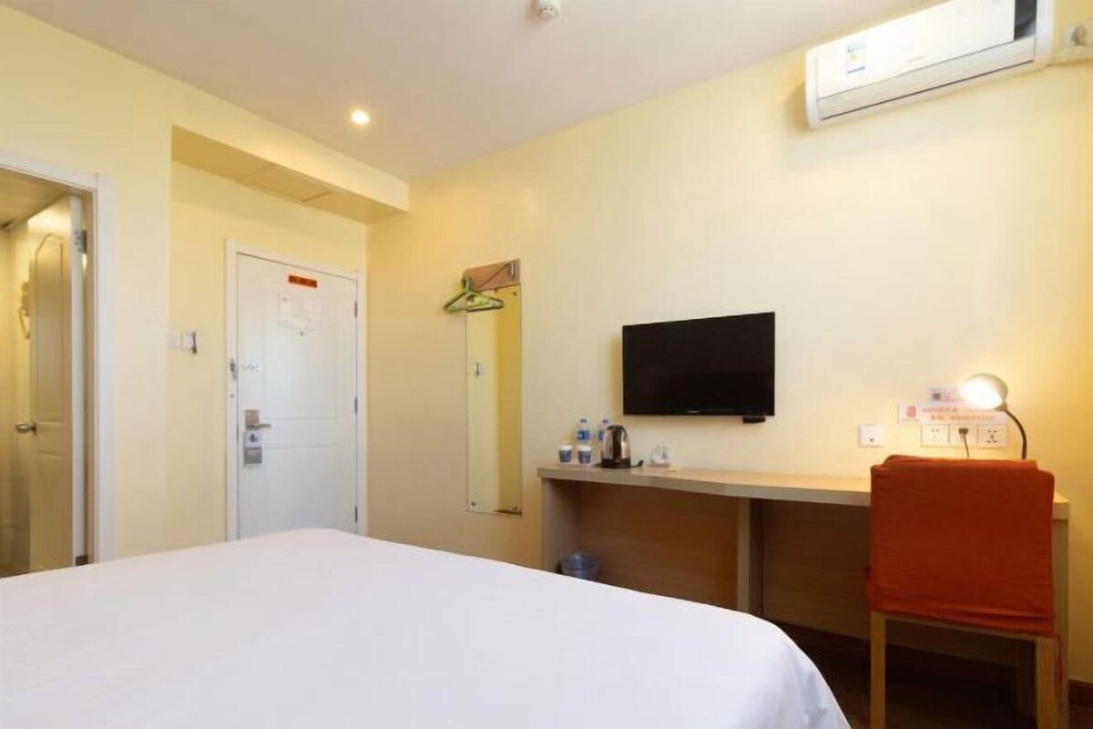 A hotel room with a bed, a desk with a chair, a television, and a mirror.
