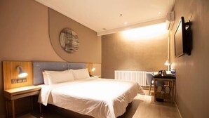Una habitación de hotel con una cama, mesitas de noche, un escritorio y un televisor montado en la pared.