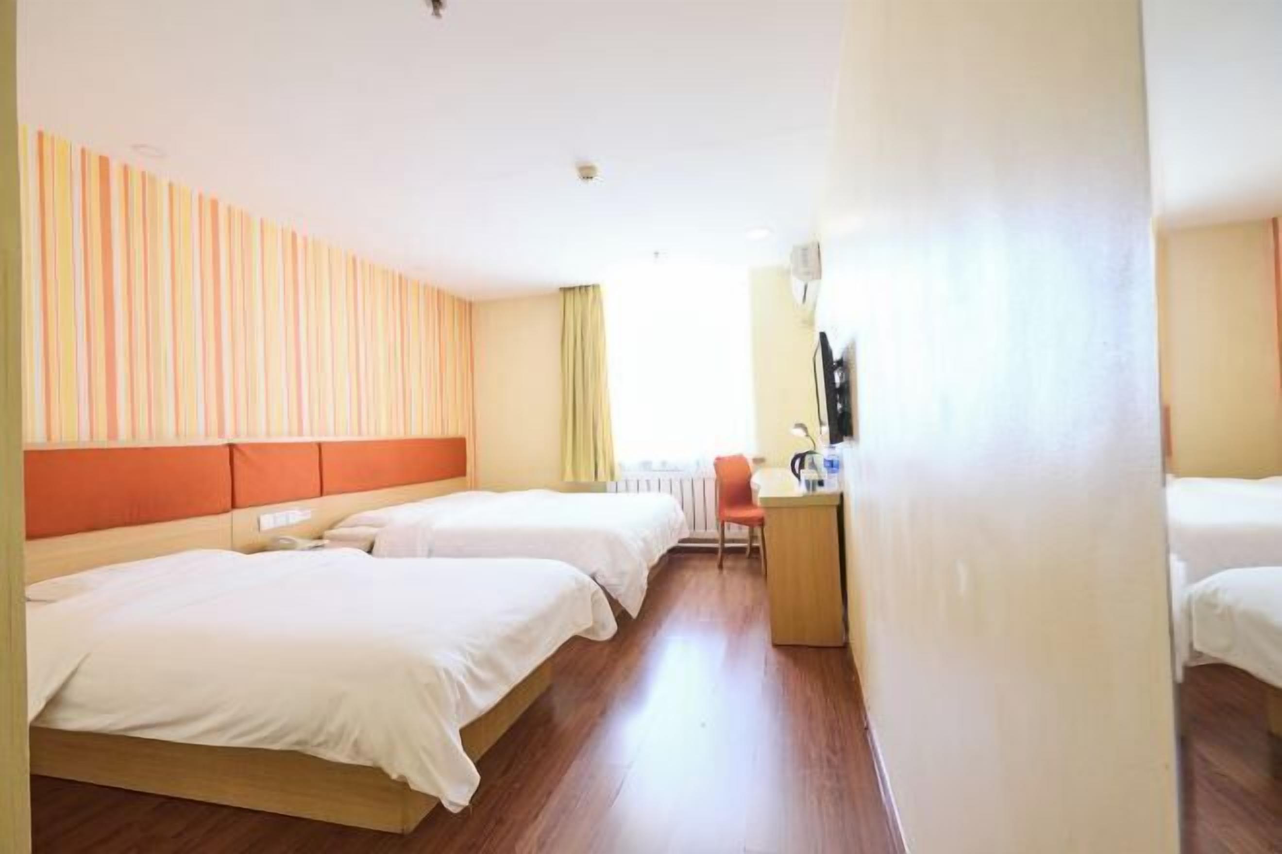 A hotel room with two beds, a desk, and a window.