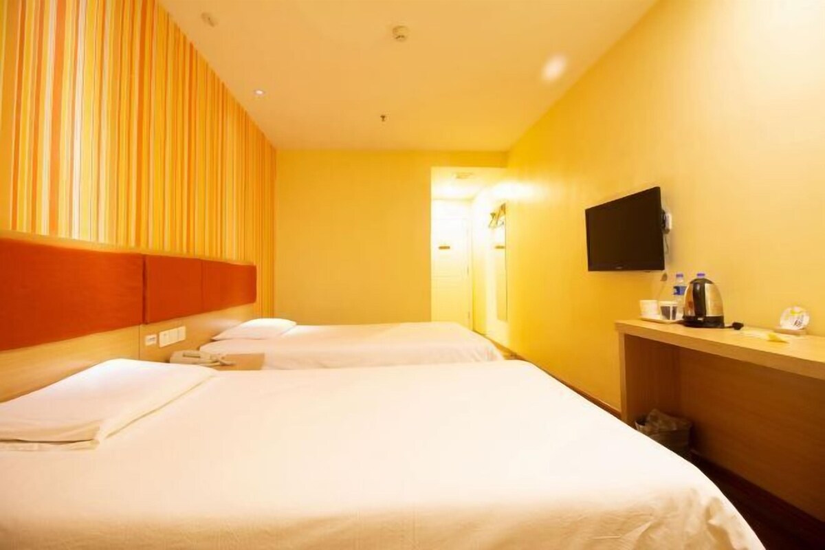 A hotel room with three beds, a television, and a small desk with a kettle.