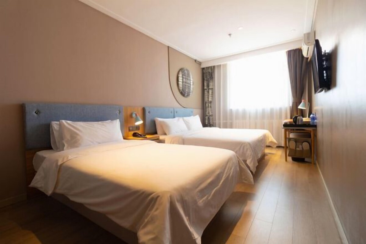 A hotel room with two beds, a round wall decoration, a TV mounted on the wall, and a window with curtains.