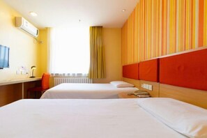 A hotel room with two beds, a desk, an air conditioner, and a window with curtains.