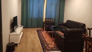 Een woonkamer met een bank, een tafeltje, een televisie en een raam met gordijnen.