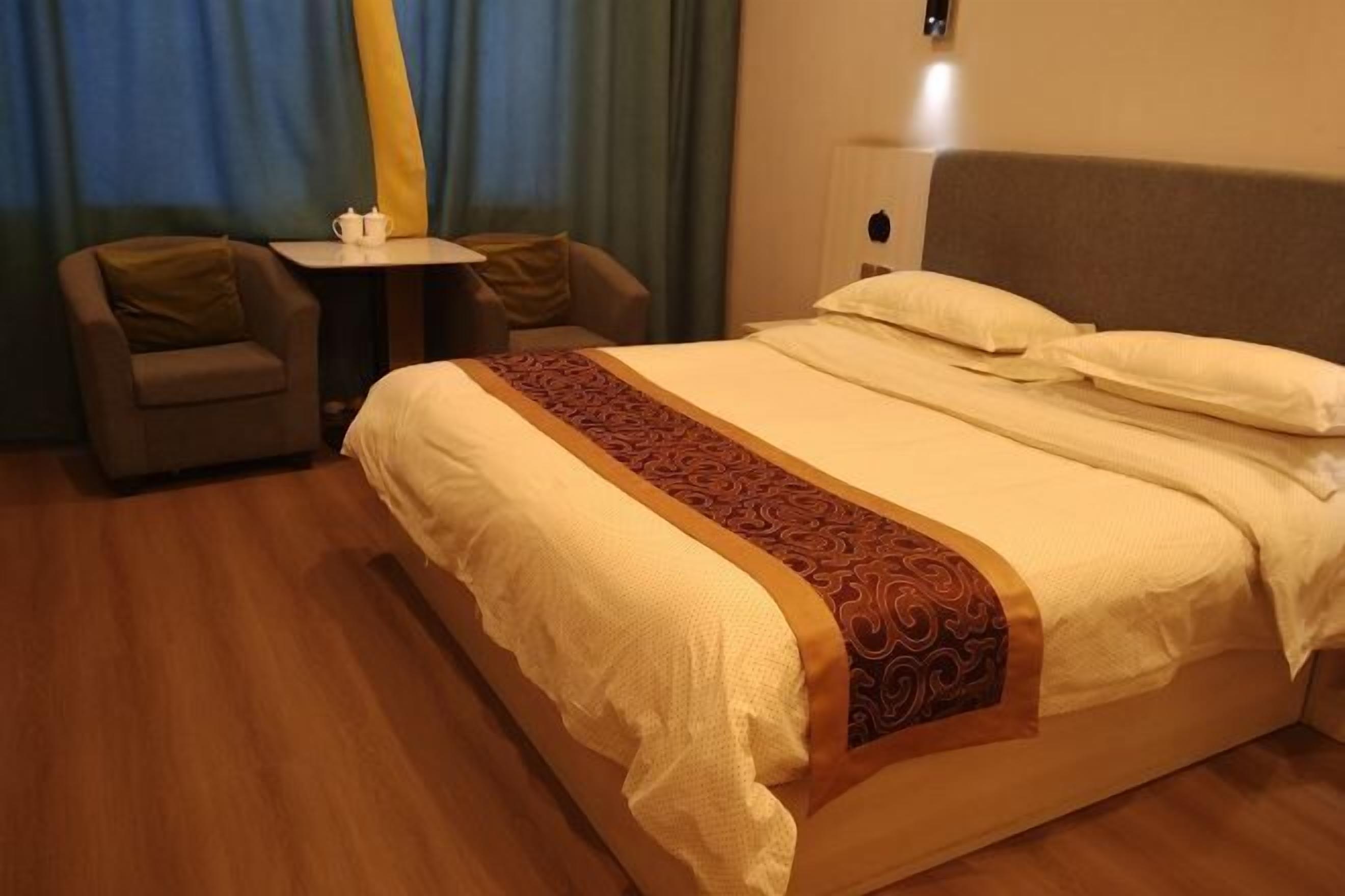 A hotel room with a bed, two armchairs, a small table, and a nightstand.