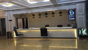A reception area with a modern design, featuring a reception desk, two black chairs, a ceiling with recessed lighting, and a television screen on the wall.