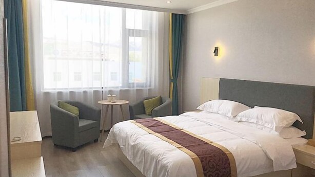 Een hotelkamer met een groot bed, een klein rond tafeltje, twee fauteuils en een raam met gordijnen.