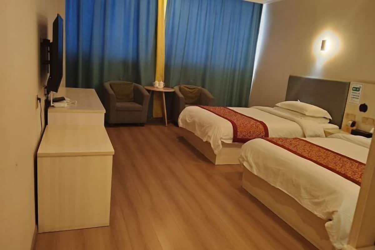 Een hotelkamer met een bureau, twee bedden, een televisie en een kleine tafel met stoelen.