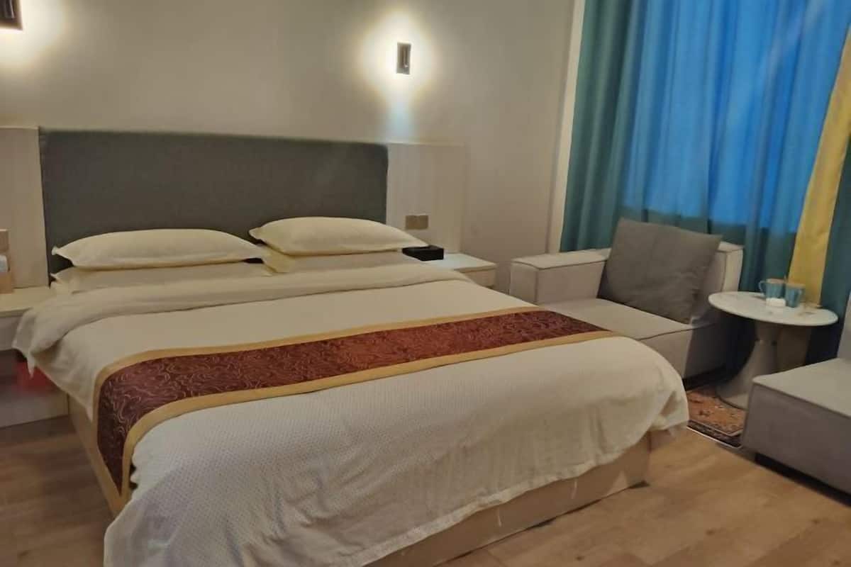 Een hotelkamer met een groot bed, twee nachtkastjes, een stoel, een klein tafeltje en een raam met gordijnen.