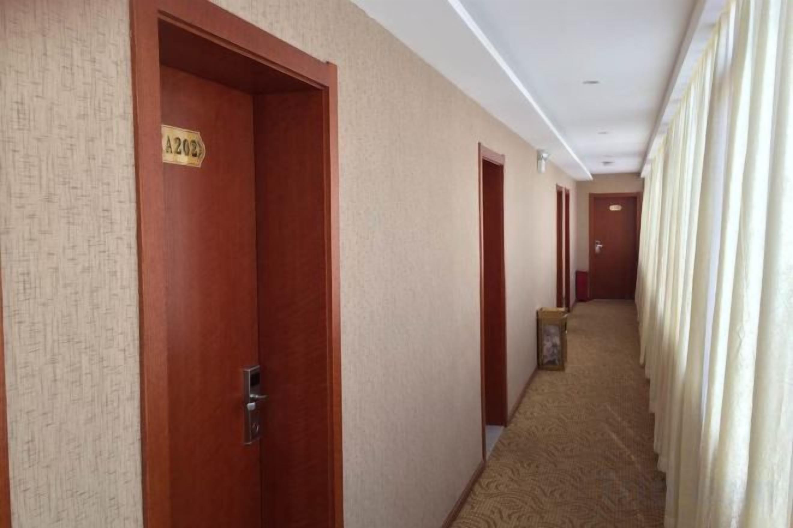 En hotellkorridor med dörrar som är märkta med rumsnummer, ett heltäckningsmatta på golvet och en enkel vägg.