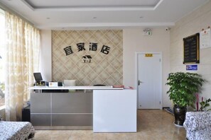 A reception desk with a sign above it, a door to the right, and a potted plant to the right of the desk. - Anning IKEA Express Hotel (Anning)