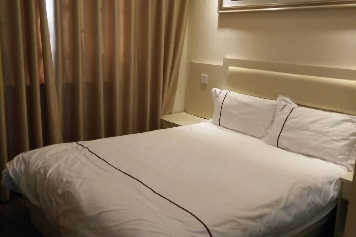 A hotel room with a bed, curtains, a nightstand, and a wall-mounted light.