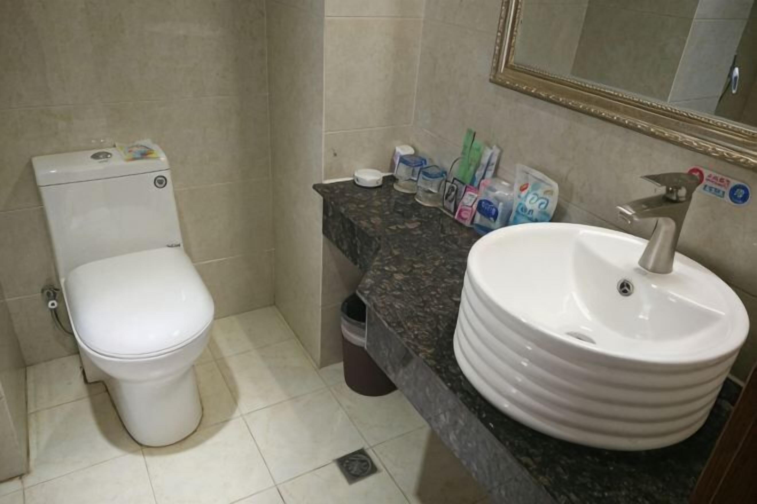 A bathroom with a toilet, sink, mirror, and toiletries on the countertop.