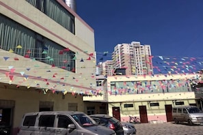 Un immeuble à étages, un parking rempli de voitures et des drapeaux triangulaires aux couleurs vives.