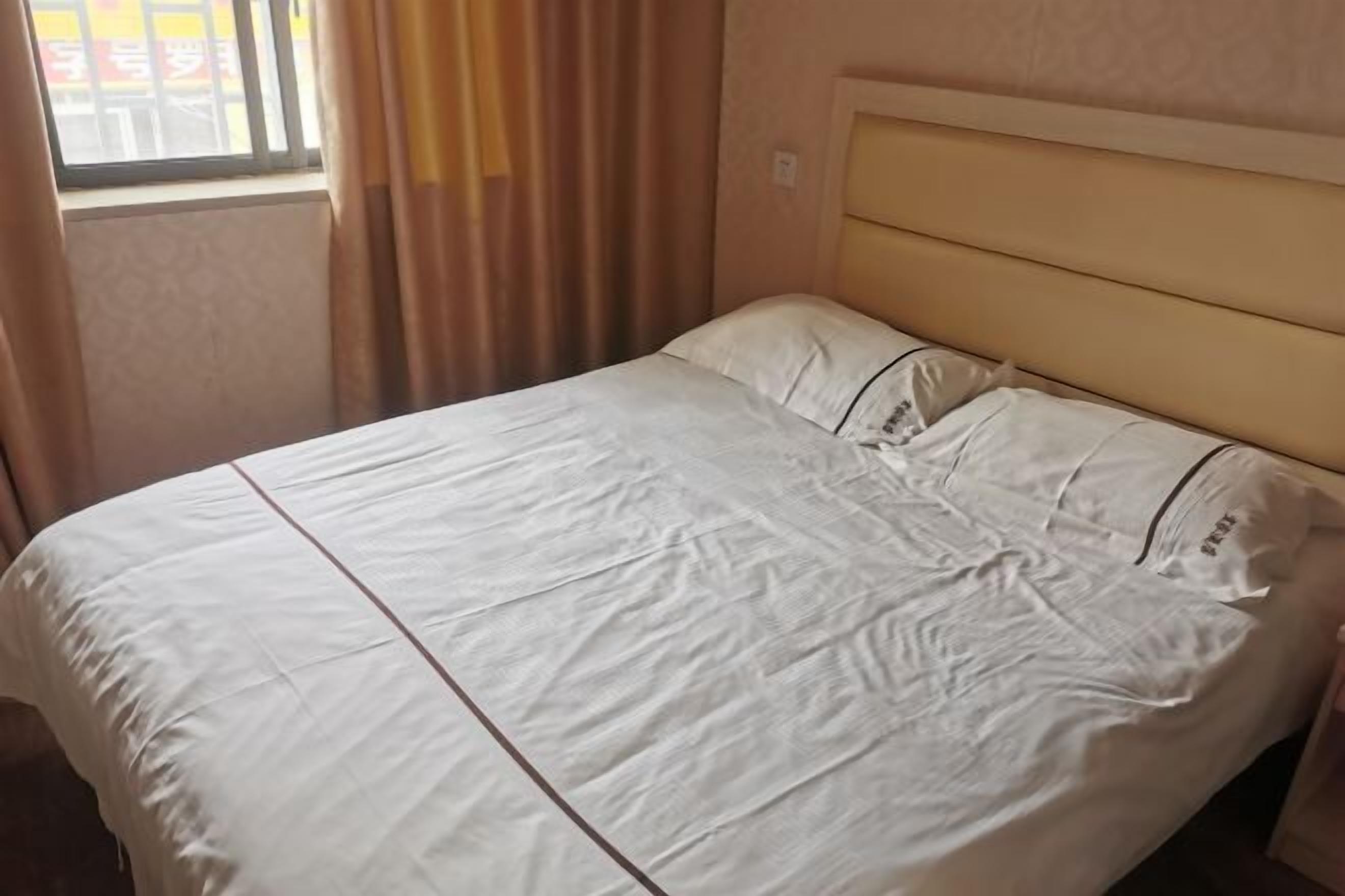Een bed met hoofdbord, gordijnen en een raam met zonwering.