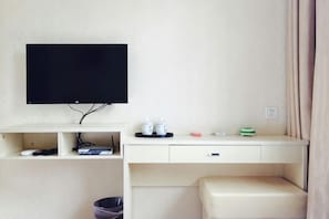 Une chambre d’hôtel équipée d’un téléviseur fixé au mur, d’un bureau avec un ordinateur, d’une poubelle et d’un petit coin salon.