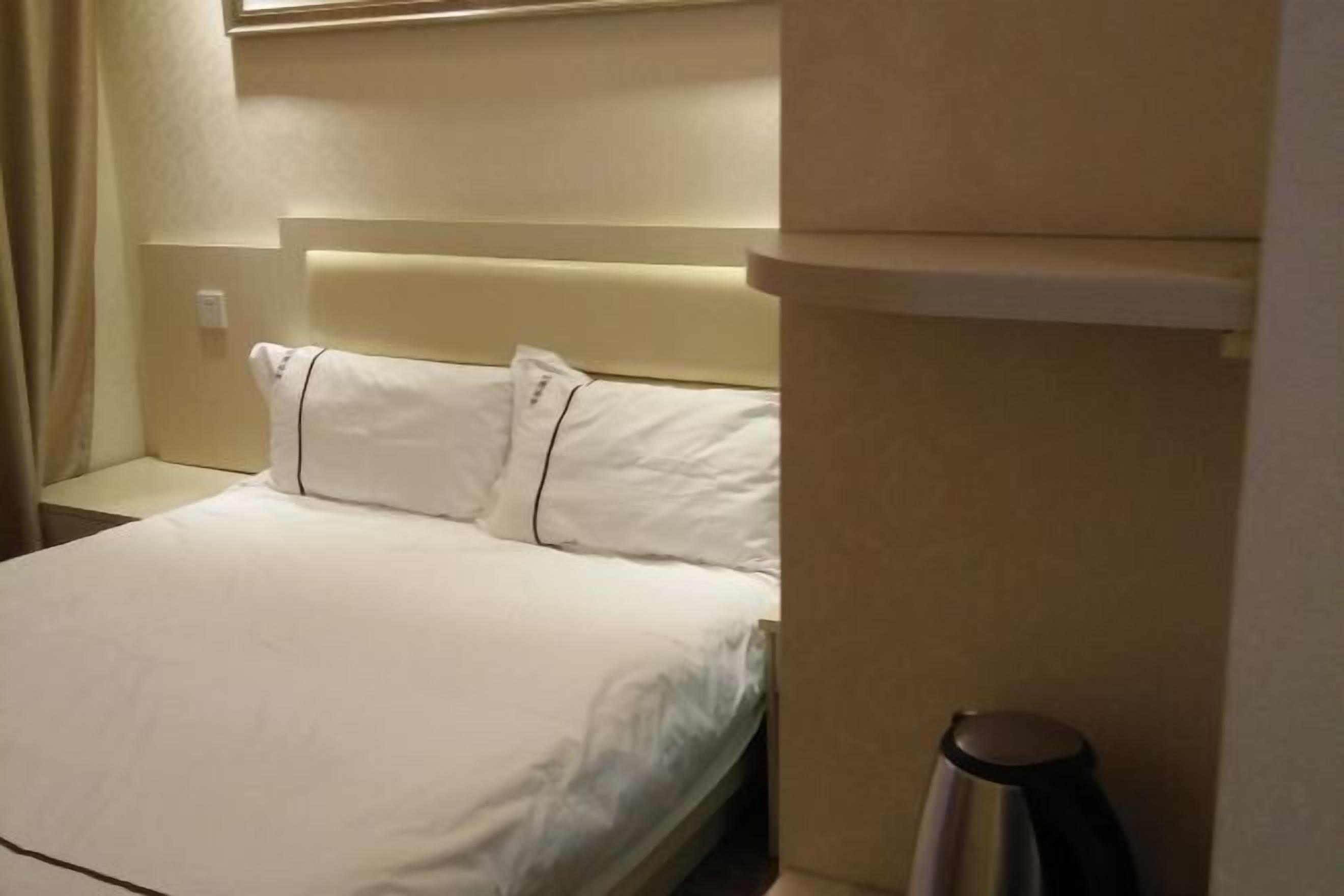 A hotel room with a bed, a nightstand, a lamp, and a wall-mounted shelf.