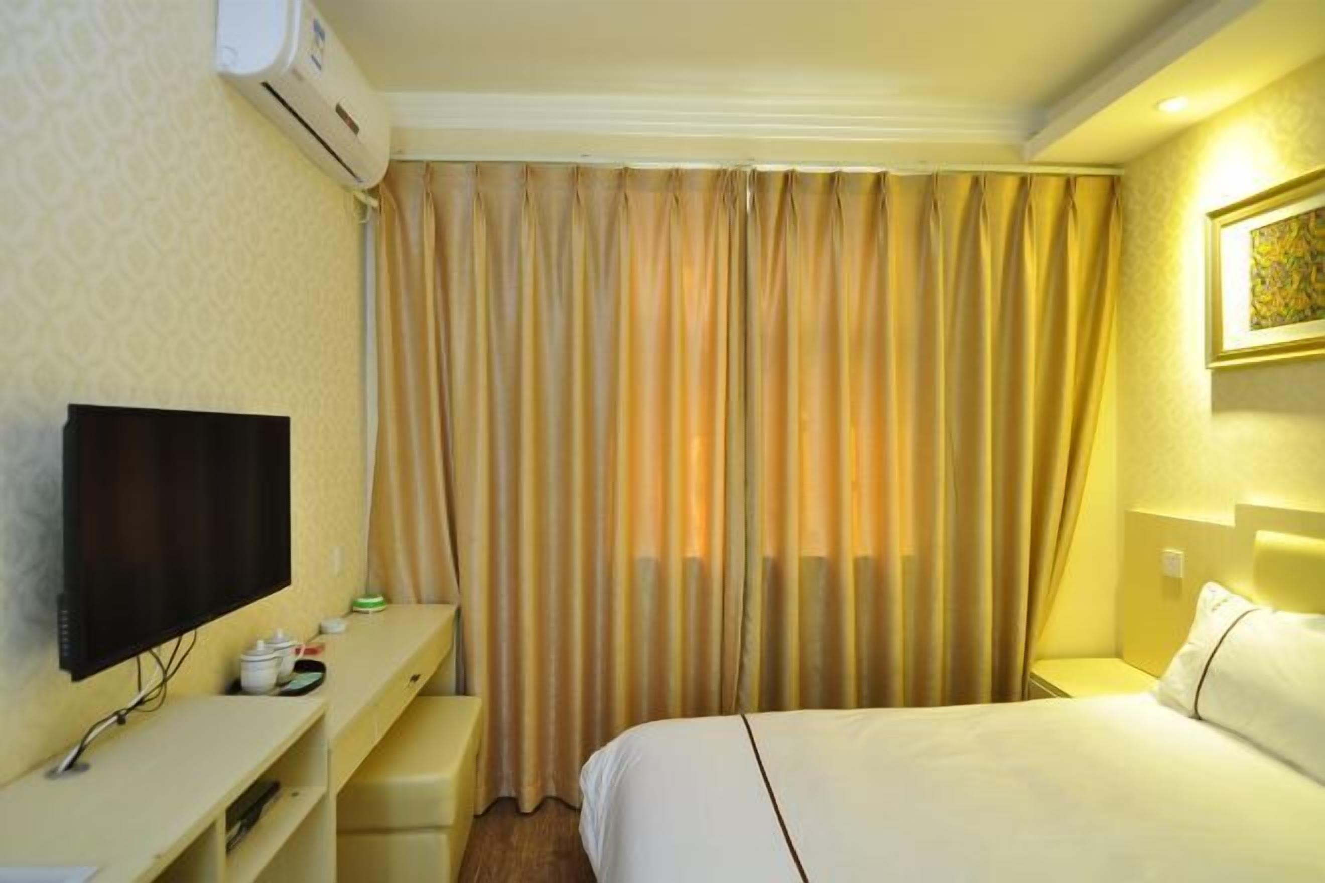 Una camera d'albergo con un letto, una TV, una scrivania e una finestra con tende.
