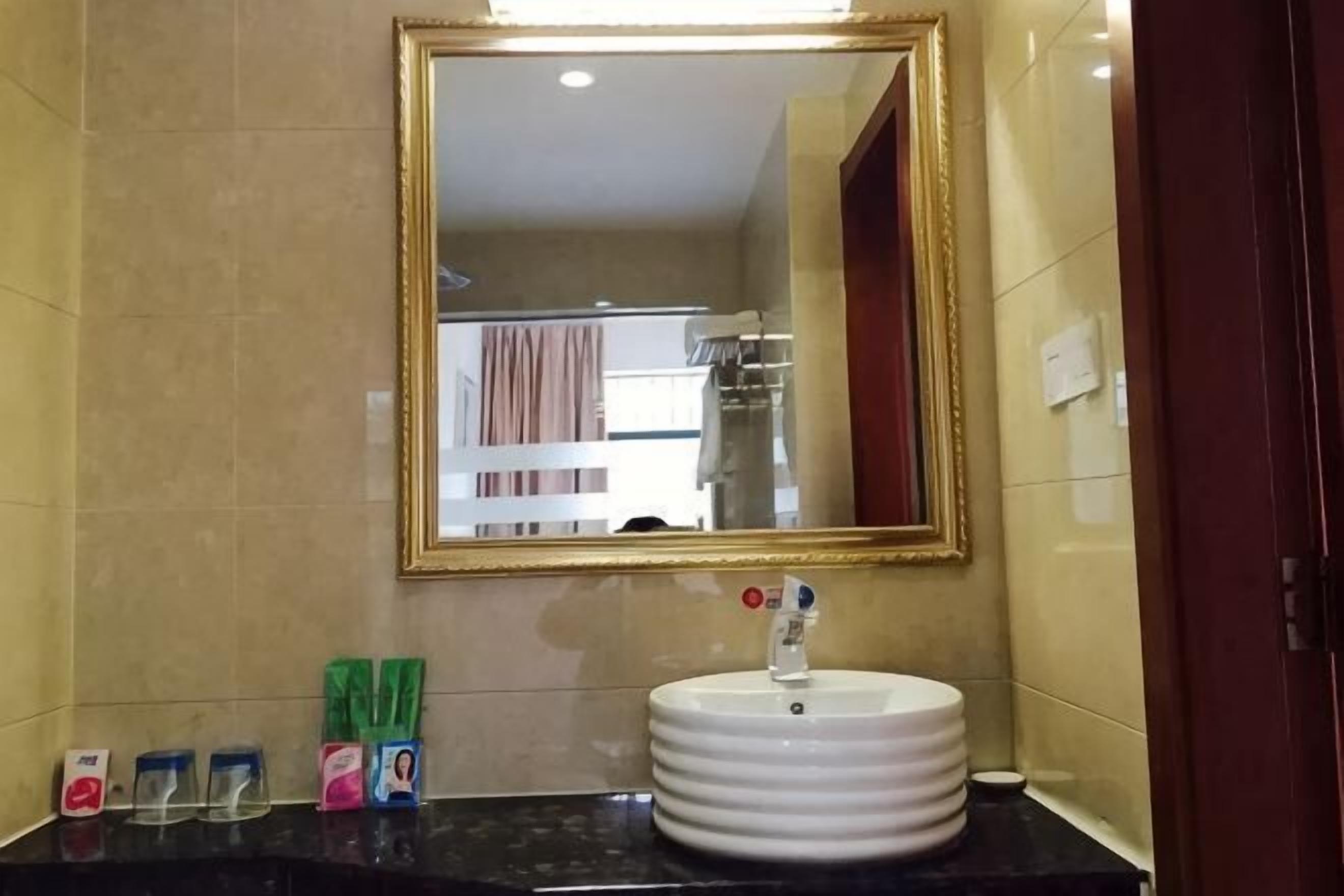 Un baño con un lavamanos blanco, un espejo con marco dorado y artículos de tocador sobre la encimera.