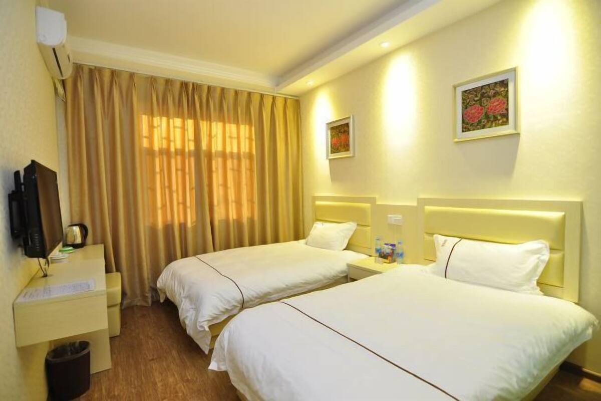 A hotel room with two beds, a desk with a chair, a trash bin, and a television.