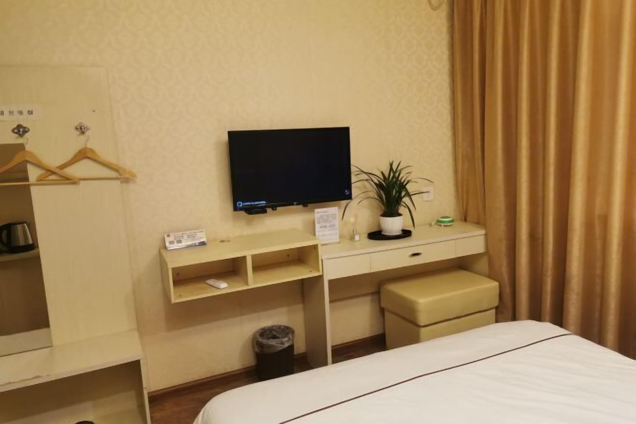 Une chambre d’hôtel comprenant un lit, un bureau avec une télévision, une petite plante et une armoire avec des cintres.