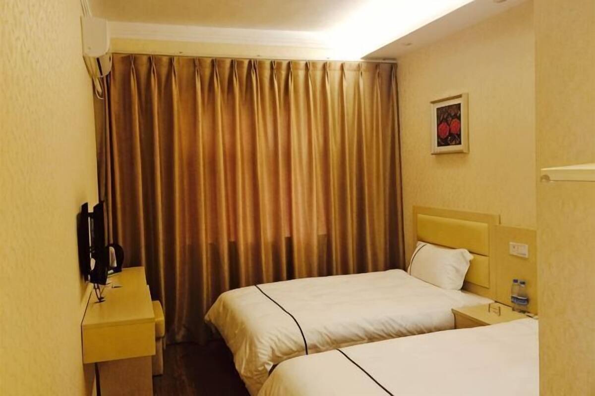 A hotel room with two beds, a desk with a telephone, and a curtain.