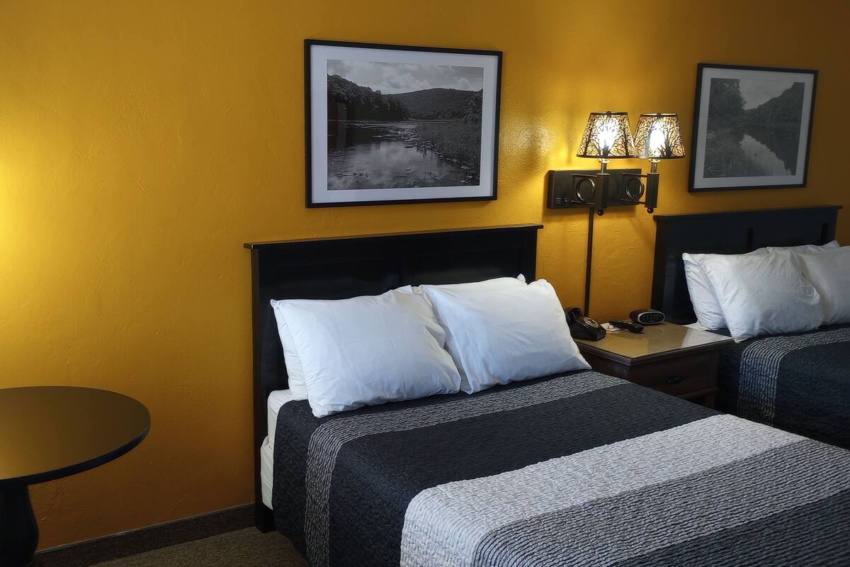 A hotel room with two beds, a round table, and two wall-mounted lamps.