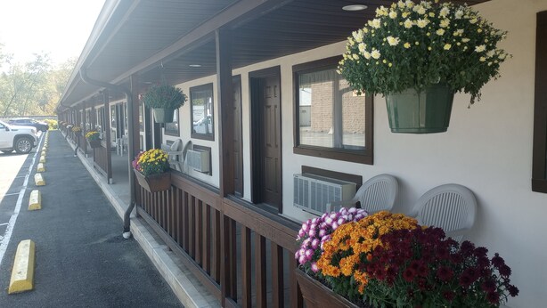 A motel with a covered porch, outdoor seating, and flower planters. - Upper Delaware Inn (Hancock)