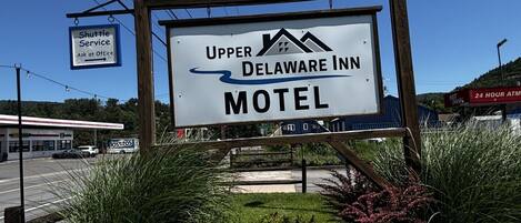 A motel sign with 'Upper Delaware Inn' and 'Motel' text, surrounded by greenery.