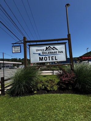 A motel sign with 'Upper Delaware Inn' and 'Motel' text, surrounded by greenery.