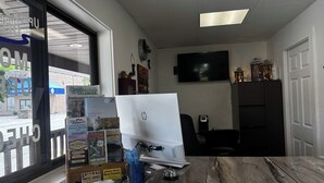 A hotel reception desk with a desktop computer, a window with a view of the outside, and various informational brochures. - Upper Delaware Inn (Hancock)
